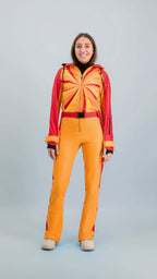 Modèle portant une combinaison de ski Hélios rouge-orange inspirée des années 80, prête pour les pistes.