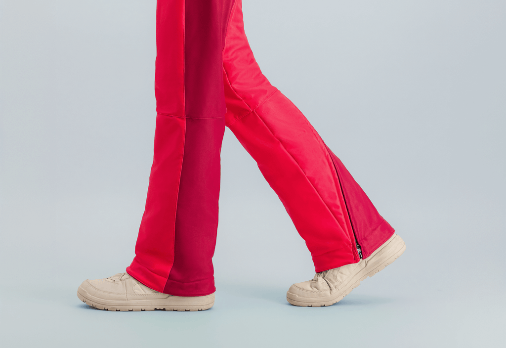 Détail de la combinaison de ski Rouge Forfait avec des jambes rouge vif et des chaussures claires sur fond neutre.