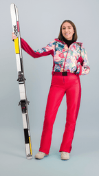 Femme portant une combinaison de ski Rouge Forfait avec skis, mettant en avant le style rétro et coloré du ski.